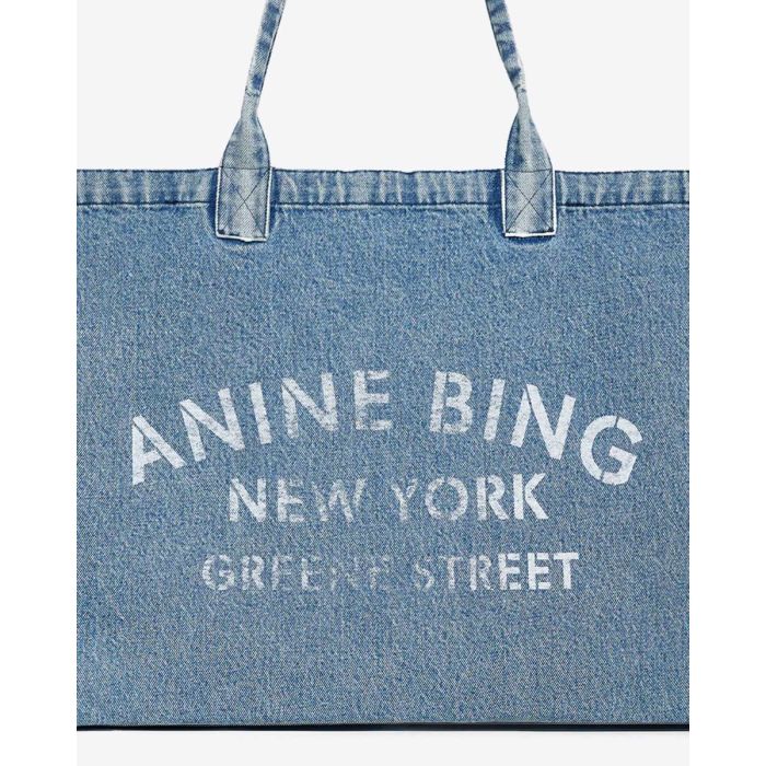 Cabas Leo Denim Tote Anine Bing en toile de coton bleu délavé. Détail de la sérigraphie blanche ANINE BING NEW YORK GREENE STREET.