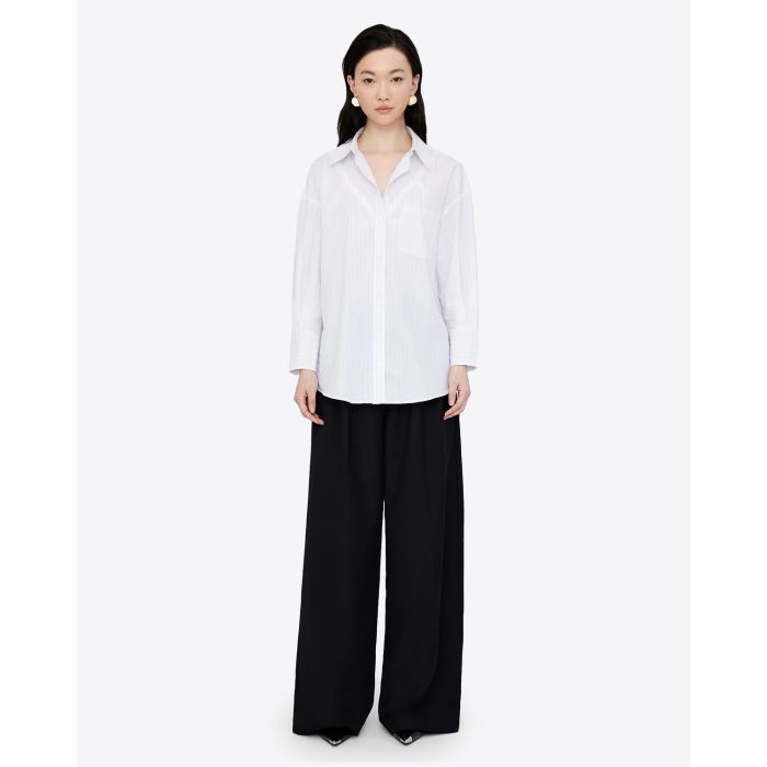 Chemise blanche manches longues Mika Anine Bing à rayures noires. Vue face. Portée avec un pantalon noir. 