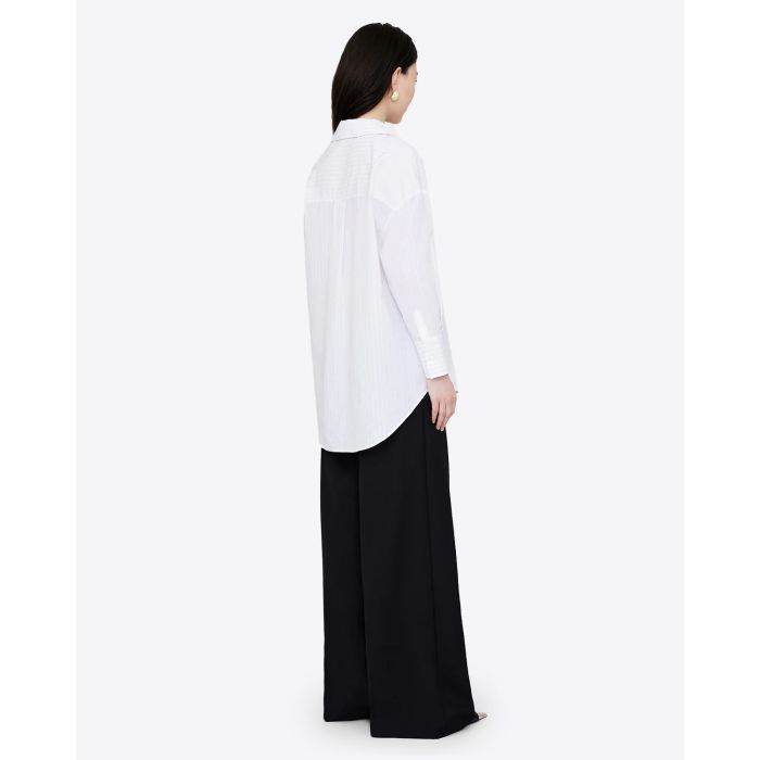 Chemise blanche manches longues Mika Anine Bing à rayures noires. Vue trois quart dos. Portée avec un pantalon noir. 