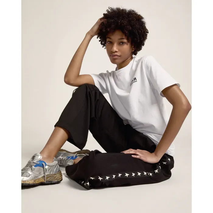 Pantalon de jogging noir avec étoiles blanches le long de la jambe Golden Goose. Porté avec un tee-shirt blanc logo.