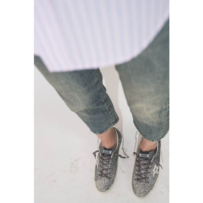 Sneakers entièrement recouvertes de paillettes argentées et noires, étoile en cuir lisse tague écritures noires sur la semelle droite beige "LOVE You To The Star And Back"  Super-star Golden Goose femme. Portées de profil avec un jean Boy Straight bleu R1