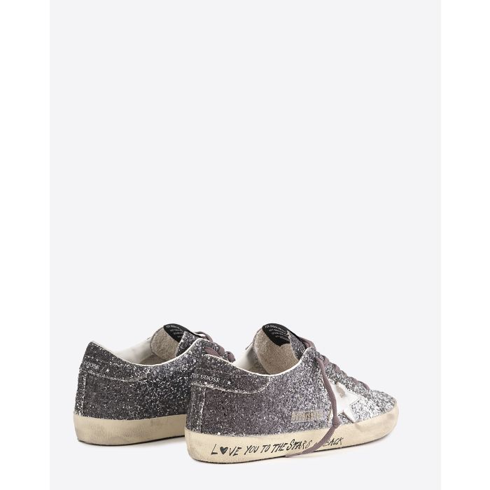 Sneakers entièrement recouvertes de paillettes argentées et noires, étoile en cuir lisse tague écritures noires su la semelle beige "L????VE You To The Star And Back"  Super-star Golden Goose femme. Face.