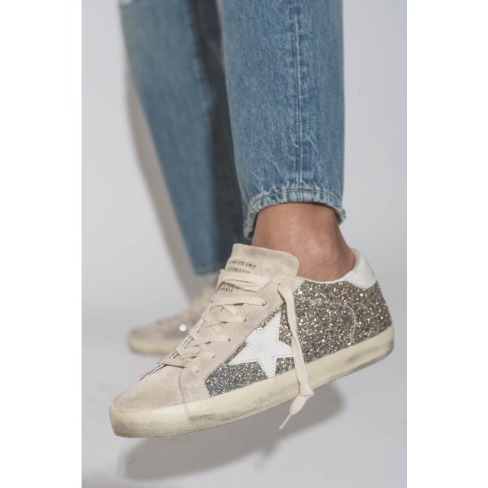 Sneakers Superstar à paillettes argent et or étoile en cuir blanc 55636 Golden Goose Femme. Porté avec un jean bleu.
