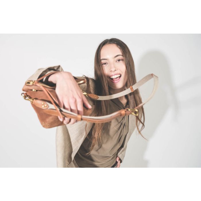 Pochette en cuir suédé caramel Lucky Jérôme Dreyfuss portée main avec une bandoulière sangle large écru Jérôme Dreyfuss. Alyssa porte une veste Ragged Oversized beige en lin R13 avec un tee-shirt sans manches Nayda kaki Isabel Marant Etoile. 