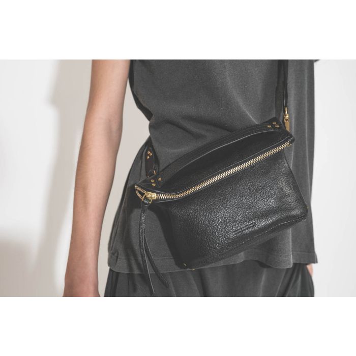 Pochette en cuir de chèvre noir grainé portée crossbody avec une bandoulière sangle large noire Jérôme Dreyfuss. Tee-shirt manches courtes Boxy Crew et pantalon sarouel en jersey noir délavé The Great. Détail de la pochette. 