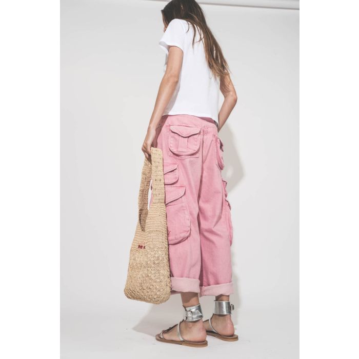 Jean taille basse oversized en toile rose multi-poches Cargo R13 denim. Porté de profil dos avec un tee-shirt blanc Little The Great, des sandales en cuir argent Caravelle K.Jacques St-Tropez et un sac en raphia naturel Praia Isabel Marant (porté main).