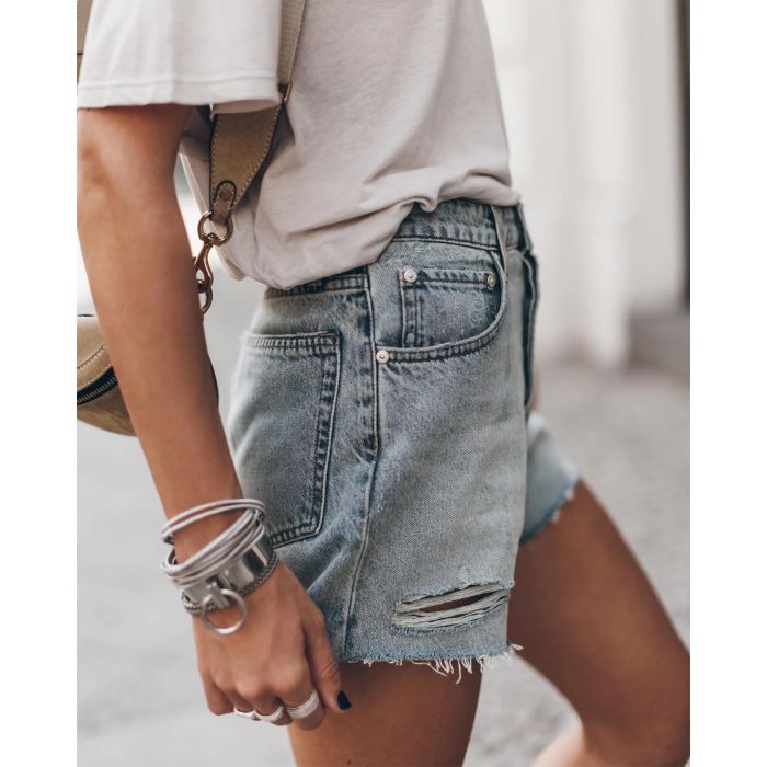 Short en jean bleu ciel usé Mikuta. Porté de profil avec un tee-shirt écru Mikuta. Bracelets en argent Mikuta.