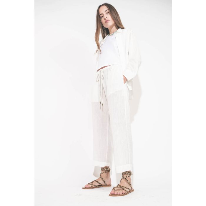 Pantalon Sarouel en voile de coton blanc Reef The Great. Porté de profil avec une chemise manches longues en voile de coton blanc et un tee-shirt sans manches Peak Shoulder The Great. Sandales en cuir pony léopard Zenobie K.Jacques St-Tropez. Collier turq