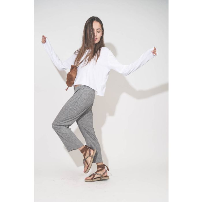 Pantalon sarouel court en jersey gris chiné The Great. Porté de profil avec une tee-shirt court manches longues blanc et des sandales en cordes tressées et ruban beige Gypsa Isabel Marant. Pochette Lucky en cuir suédé caramel portée crossbody avec une san