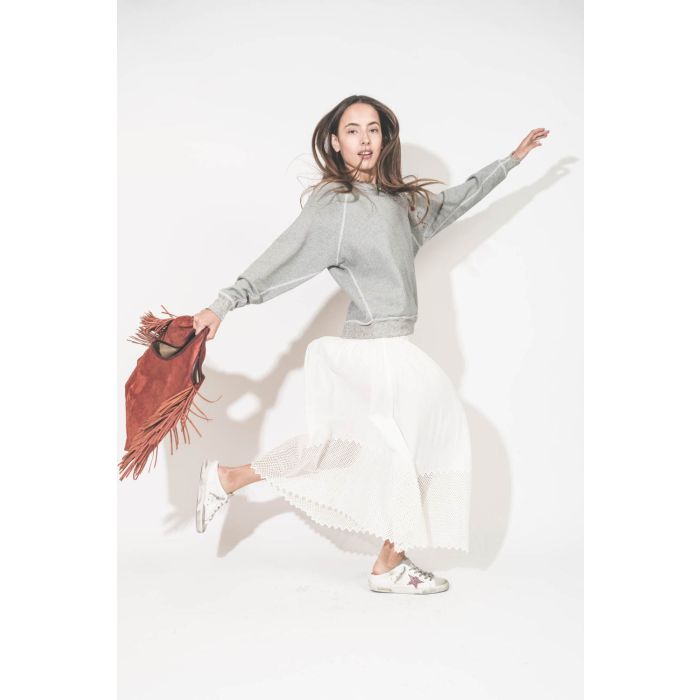 Jupe longue en coton et nid d'abeille placé sur le bas de la jupe blanche The Canary Skirt The Great. Portée de profil avec un sweat-shirt gris chiné College The Great et des sneakers Super Star sabot Golden Goose. Cabas à franges en cuir Terracotta Paco 