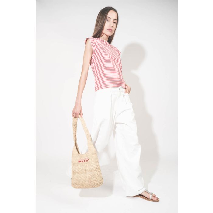 Tee-shirt manches courtes raccourcies en coton rayé rouge et blanc Peak Shoulder The Great. Porté de profil avec un jean large blanc Georgia Denimist et des sandales en cuir argent Caravelle K.Jacques St-Tropez. Panier en osier naturel Praia Isabel Marant