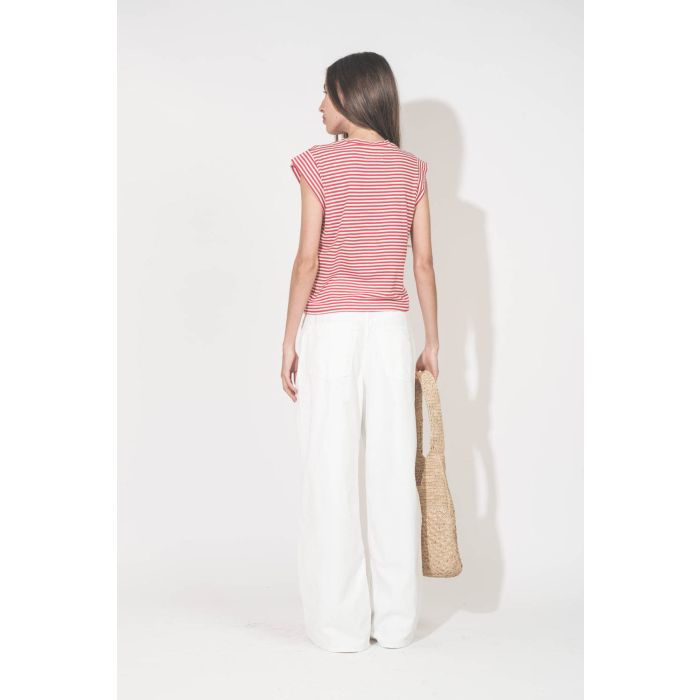 Tee-shirt manches courtes raccourcies en coton rayé rouge et blanc Peak Shoulder The Great. Porté de dos avec un jean large blanc Georgia Denimist et des sandales en cuir argent Caravelle K.Jacques St-Tropez. Panier en osier naturel Praia Isabel Marant.