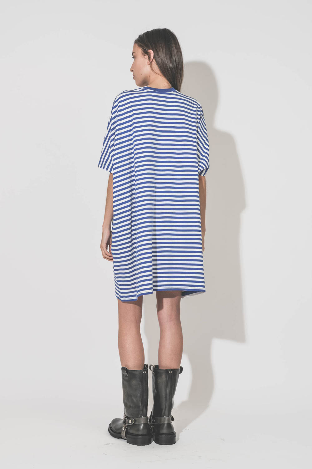 Robe manches courtes oversized en jersey de coton rayée bleu et blanche mini poche poitrine Denimist. Porté de dos avec des bottes de biker en cuir noir Kurt Golden Goose.  