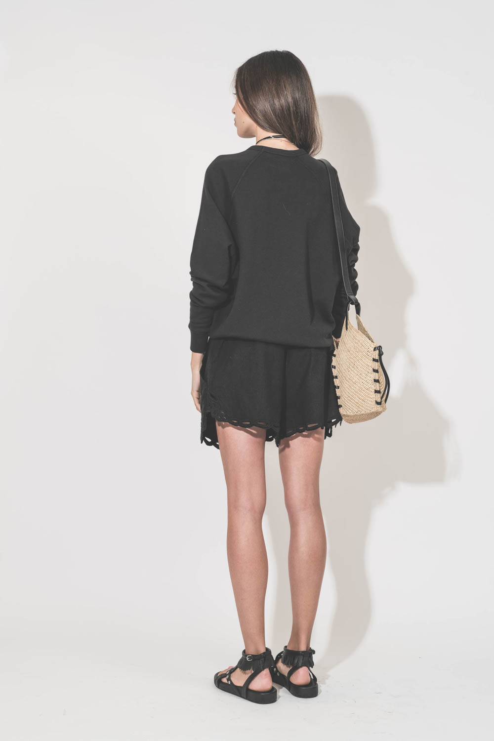 Short court en coton et dentelle ajourée noire Safa Marant Etoile. Porté de dos avec un sweat-shirt classique noir College The Great et des sandales cloutées en cuir noir Silya Isabel Marant. Panier en osier naturel et noir Tampa Mini Isabel Marant. Sauto