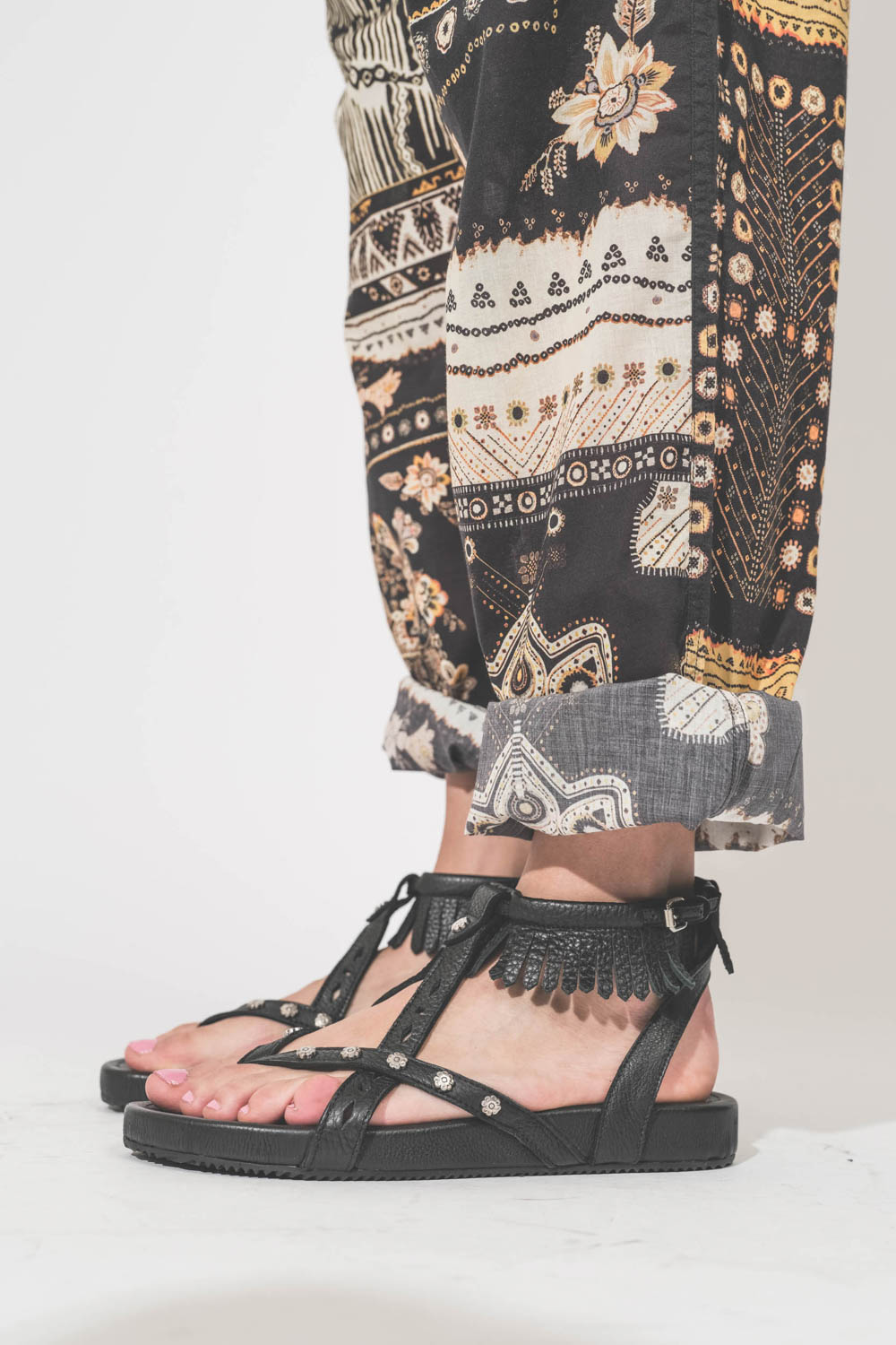 Sandales en cuir noir clouté bride à franges autour de la cheville Silya Isabel Marant. Porté de profil avec un pantalon en voile de coton imprimé Fedora Marant Etoile.