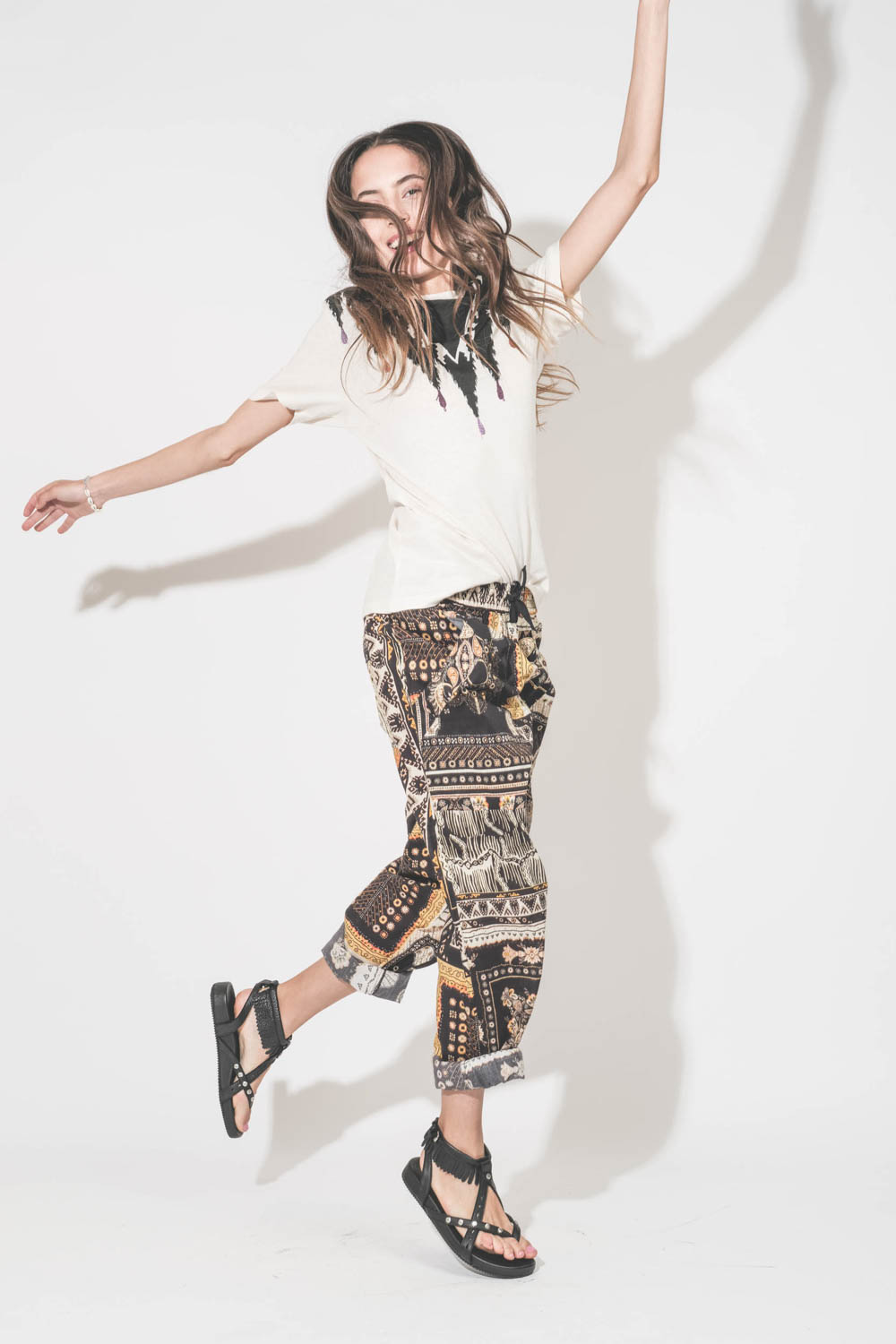 Sandales en cuir noir clouté bride à franges autour de la cheville Silya Isabel Marant. Porté avec  un tee-shirt écru imprimé placé Zewel Marant Etoile et un pantalon en voile de coton imprimé Fedora Marant Etoile.