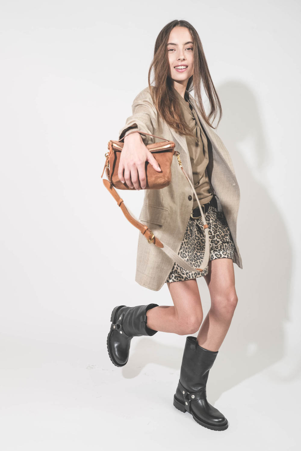 Pochette en cuir suédé caramel Lucky Jérôme Dreyfuss portée main avec une bandoulière sangle large écru Jérôme Dreyfuss. Alyssa porte une veste Ragged Oversized beige en lin R13, un tee-shirt Nayda kaki Marant Etoile et un short en toile léopard Pocket R1