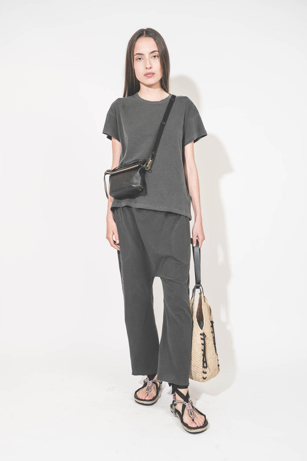 Pochette en cuir de chèvre noir grainé portée crossbody avec une bandoulière sangle large noire Jérôme Dreyfuss. Tee-shirt manches courtes Boxy Crew et pantalon sarouel en jersey noir délavé The Great. Sandales en cordes tressées et ruban noir Gypsa Isabe