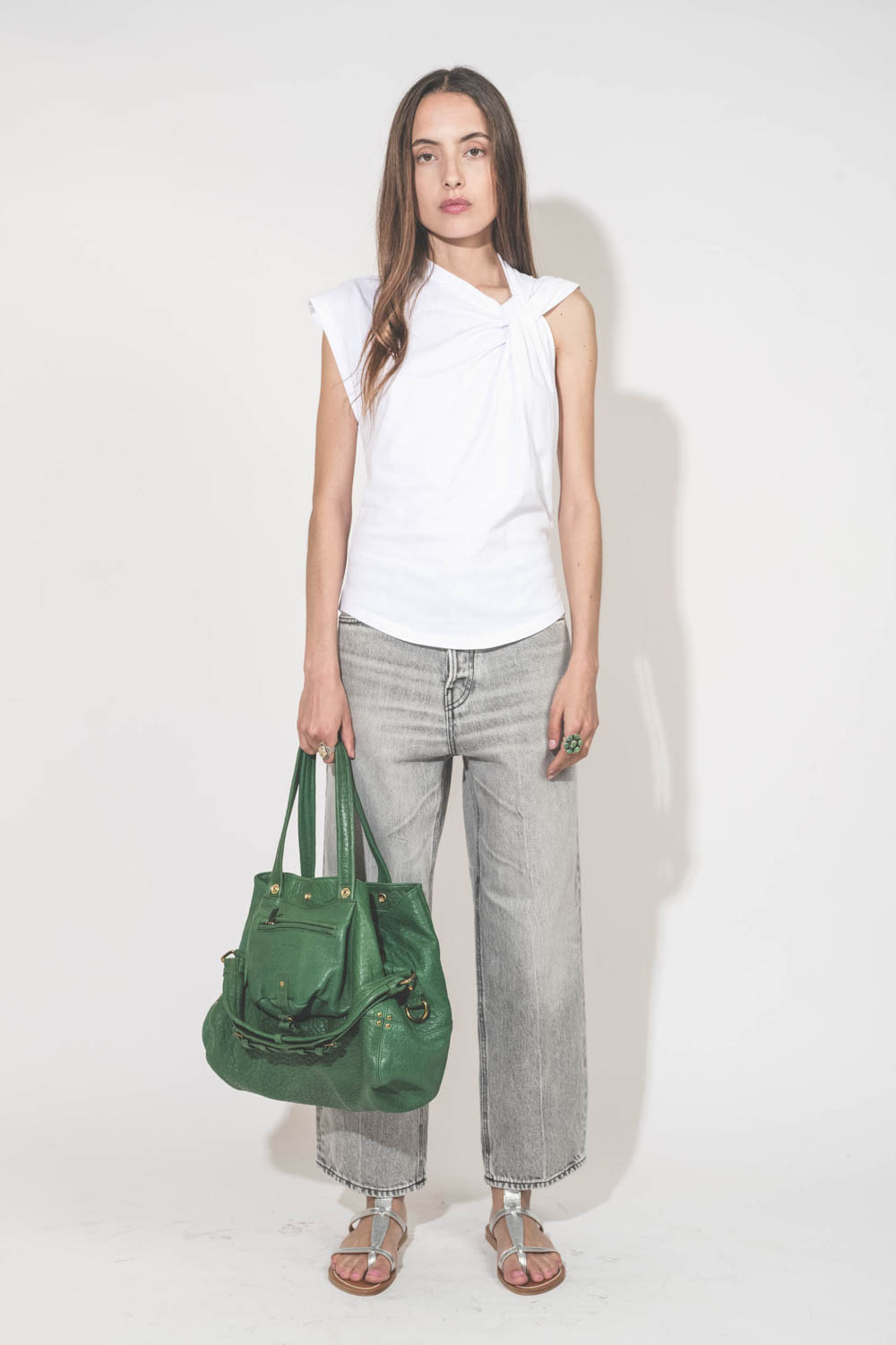 Sac forme cabas en cuir vert gazon Billy M Jérôme Dreyfuss. Porté main de face avec un tee-shirt sans manches blanc Nayda Marant Etoile et un jean large gris Betty Haikure. Sandales plates en cuir argent Caravelle K.Jacques St-Tropez. Bagues Harpo en arge