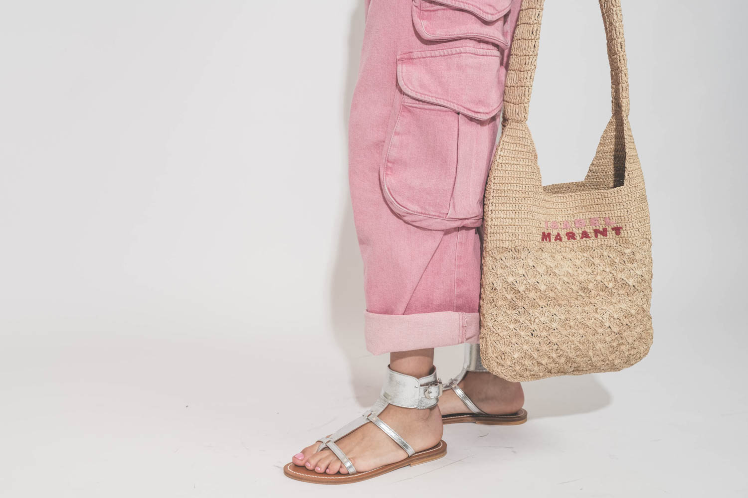 Sandales plates bracelet de cheville en cuir argent Caravelle K.Jacques St-Tropez. Porté avec un jean rose Cargo multi-poches R13 et un panier en raphia naturel logo rose et rouge Isabel Marant. 