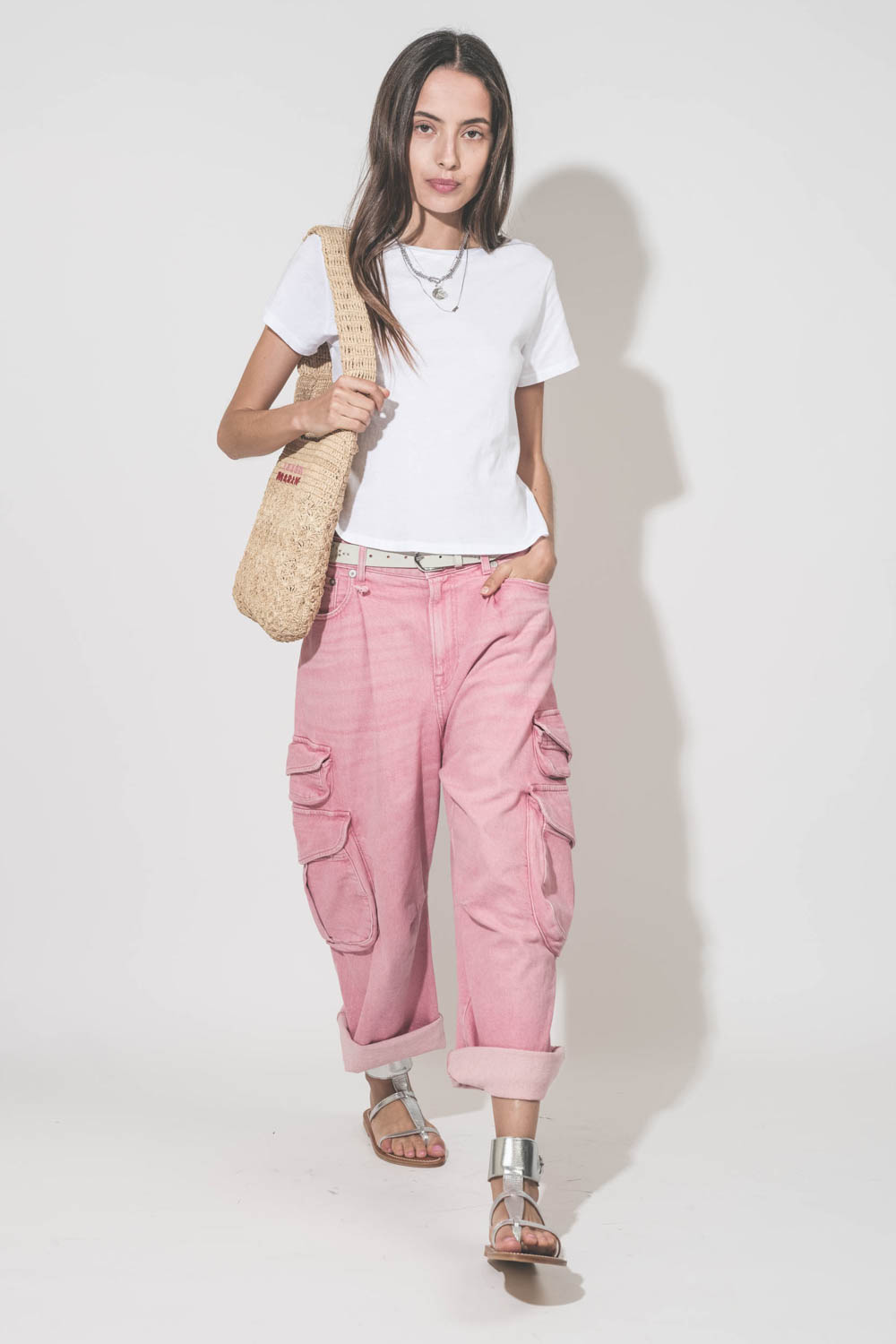 Sandales plates bracelet de cheville en cuir argent Caravelle K.Jacques St-Tropez. Portées avec un tee-shirt blanc Little The Great, un jean Cargo rose R13, une ceinture en cuir blanc Liliana Isabel Marant, un panier en raphia naturel porté sur l'épaule e