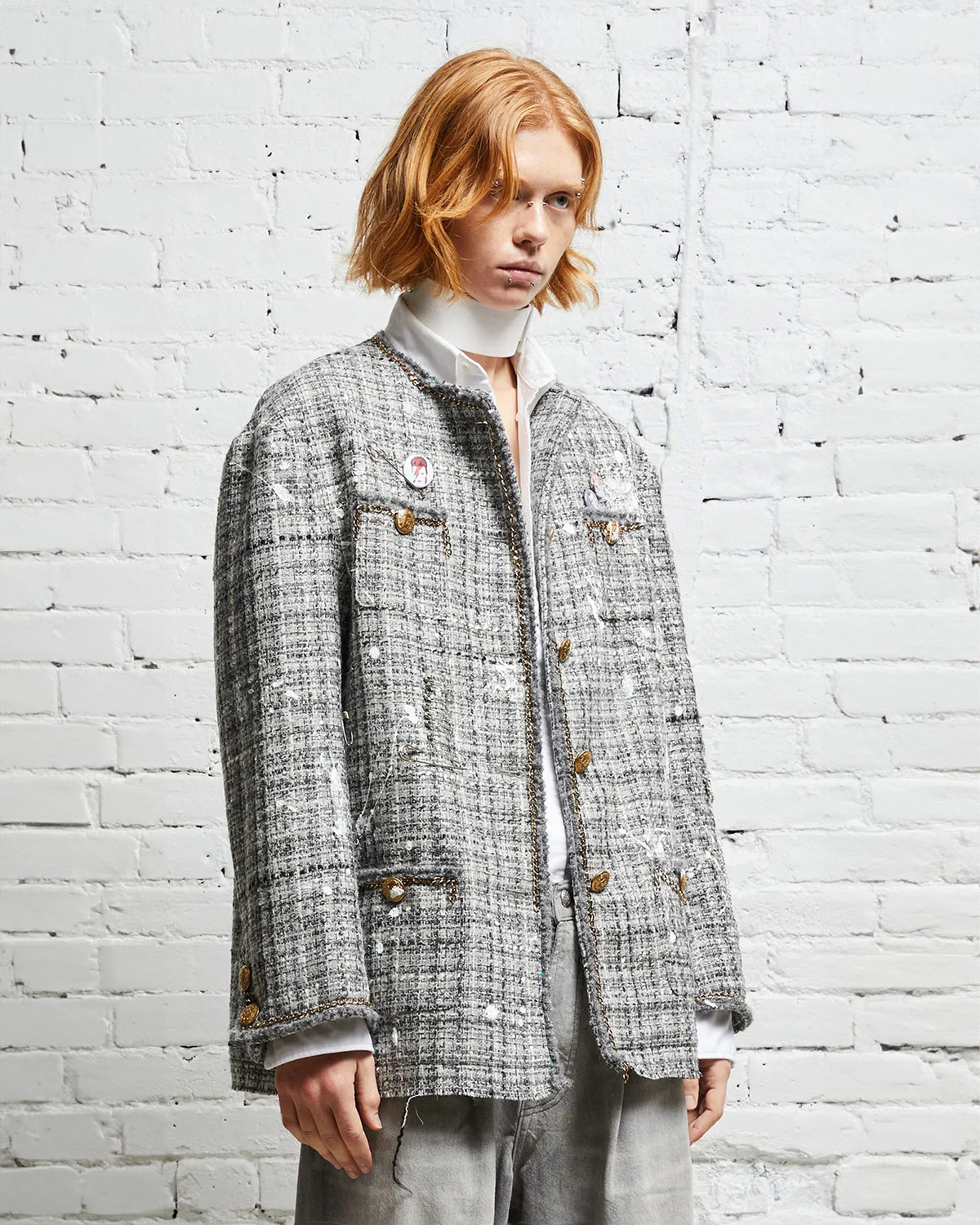 Veste oversized en tweed gris et taches de peinture avec des chaines, épingles à nourrice et badges R13. Porté de profil. 