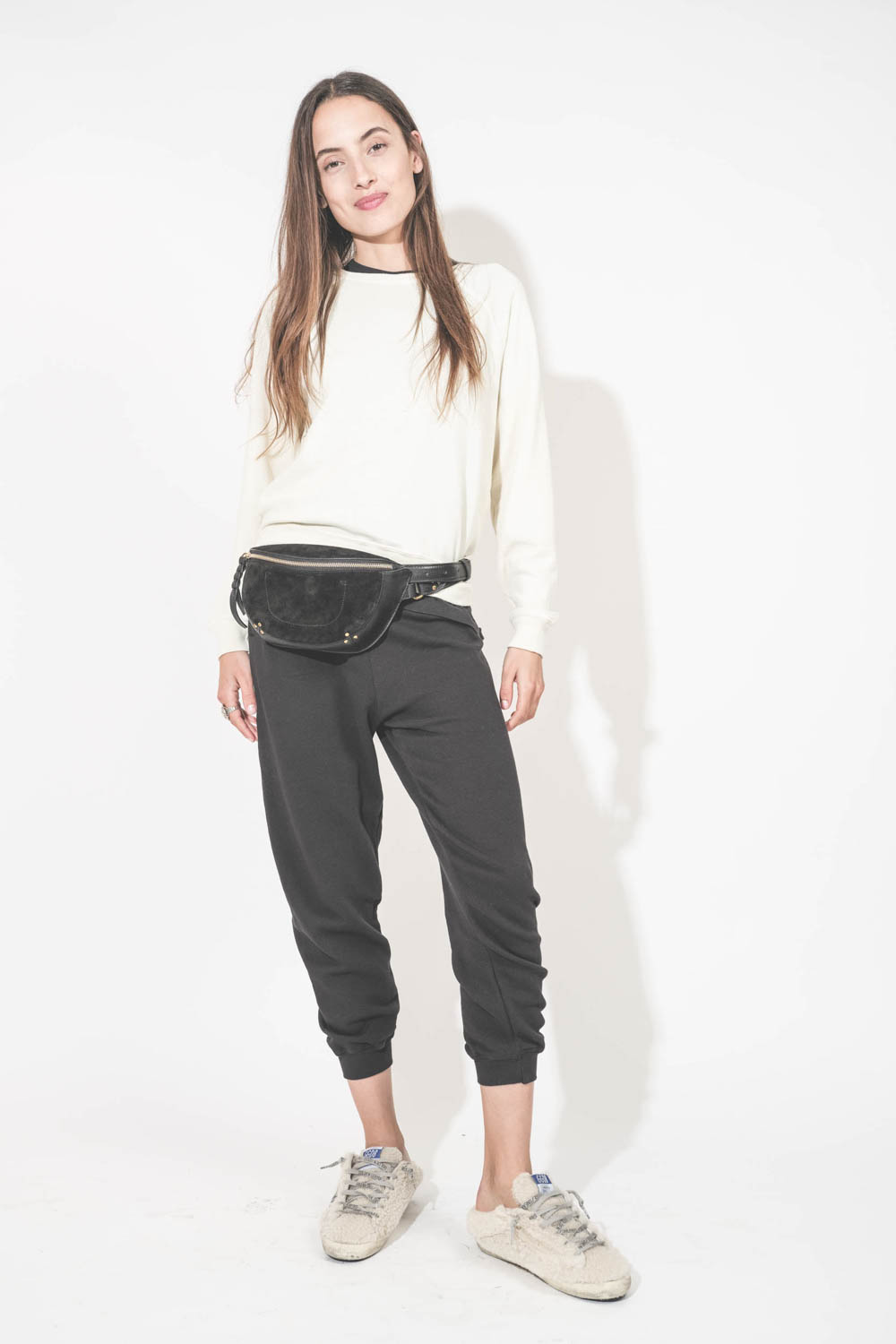 Pantalon de jogging taille basse à nouer sur les hanches resserré en bas bord côte noir The Cropped Sweatpant The Great. Porté de face avec un sweat-shirt Shrunken écru The Great et des sneakers Super Star sabot en fourrure écru 10757 Golden Goose. Sac li