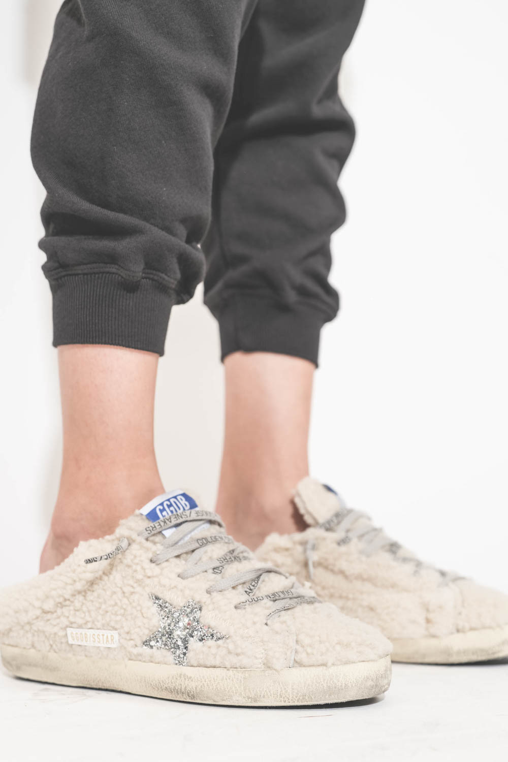 Pantalon de jogging taille basse à nouer sur les hanches resserré en bas bord côte noir The Cropped Sweatpant The Great. Détail du bas. Porté avec des sneakers Super Star sabot en fourrure écru 10757 Golden Goose. 