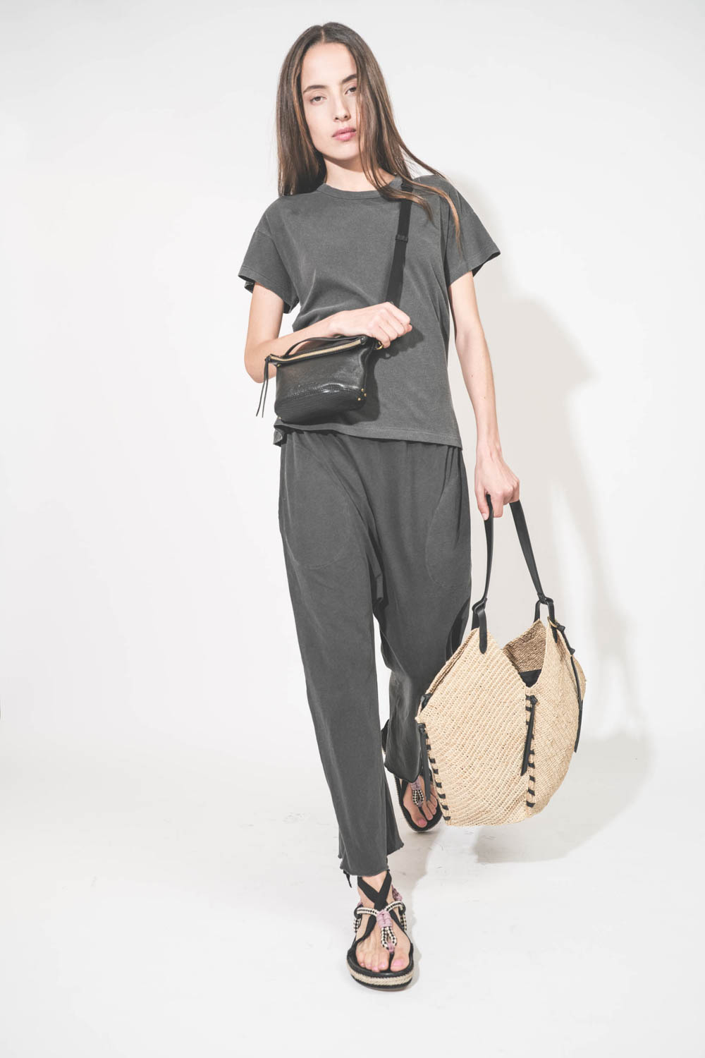 Pantalon sarouel court en jersey noir délavé The Great. Porté de face en marchant avec un tee-shirt manches courtes noir délavé Boxy Crew The Great et des sandales en cordes tressées avec ruban Gypsa noir Isabel Marant. Pochette Lucky en cuir noir avec un