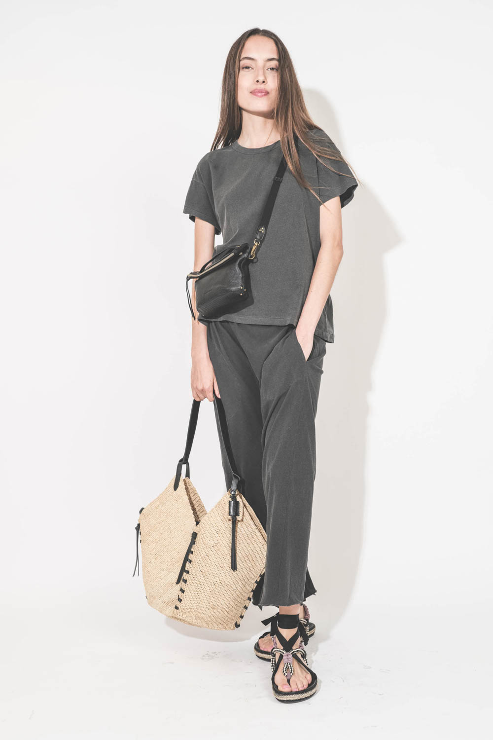Pantalon sarouel court en jersey noir délavé The Great. Porté main dans la poche avec un tee-shirt manches courtes noir délavé Boxy Crew The Great et des sandales en cordes tressées avec ruban Gypsa noir Isabel Marant. Pochette Lucky en cuir noir avec une