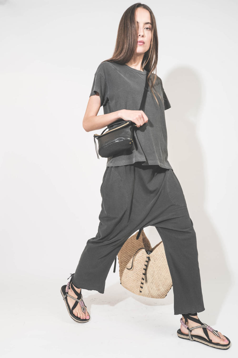Pantalon sarouel court en jersey noir délavé The Great. Porté de profil avec un tee-shirt manches courtes noir délavé Boxy Crew The Great et des sandales en cordes tressées avec ruban Gypsa noir Isabel Marant. Pochette Lucky en cuir noir avec une bandouli