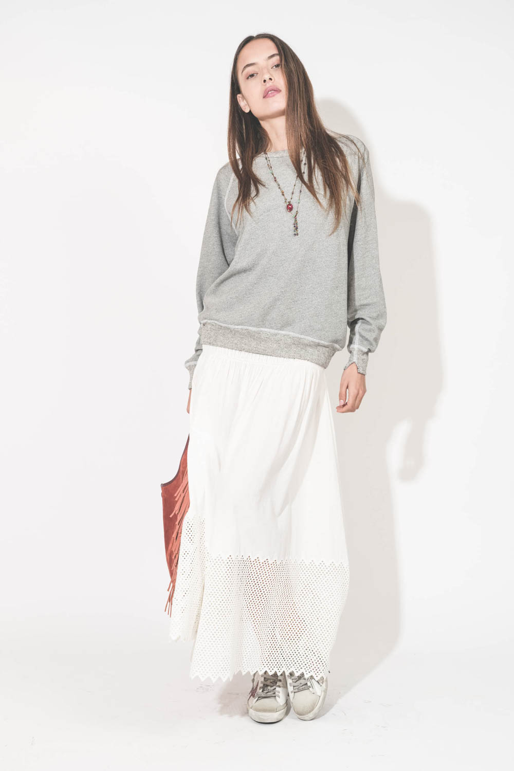 Jupe longue en coton et nid d'abeille placé sur le bas de la jupe blanche The Canary Skirt The Great. Portée de face avec un sweat-shirt gris chiné College The Great et des sneakers Super Star sabot Golden Goose. Cabas à franges en cuir Terracotta Paco Jé