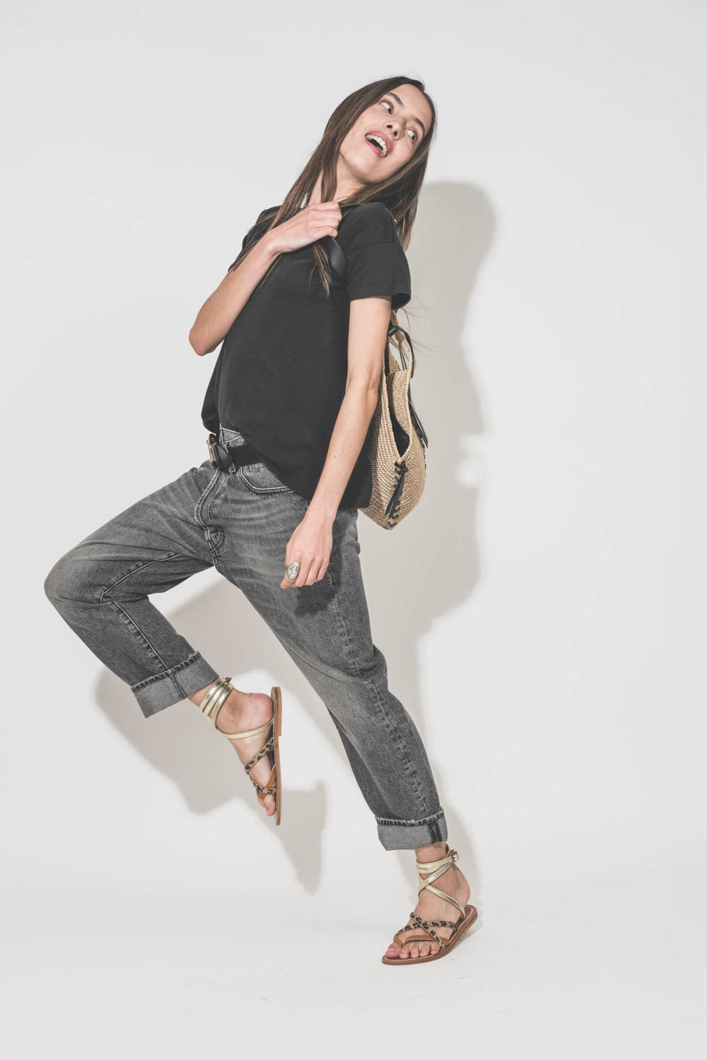 Tee-shirt manches courtes noir Boxy Crew The Great. Porté de profil avec un jean Crossover Leyton Black et des sandales plates Zenobie Pul naturel léopard platine K.Jacques Saint-Tropez. Ceinture en cuir noir Dara Isabel Marant et panier en osier naturel 