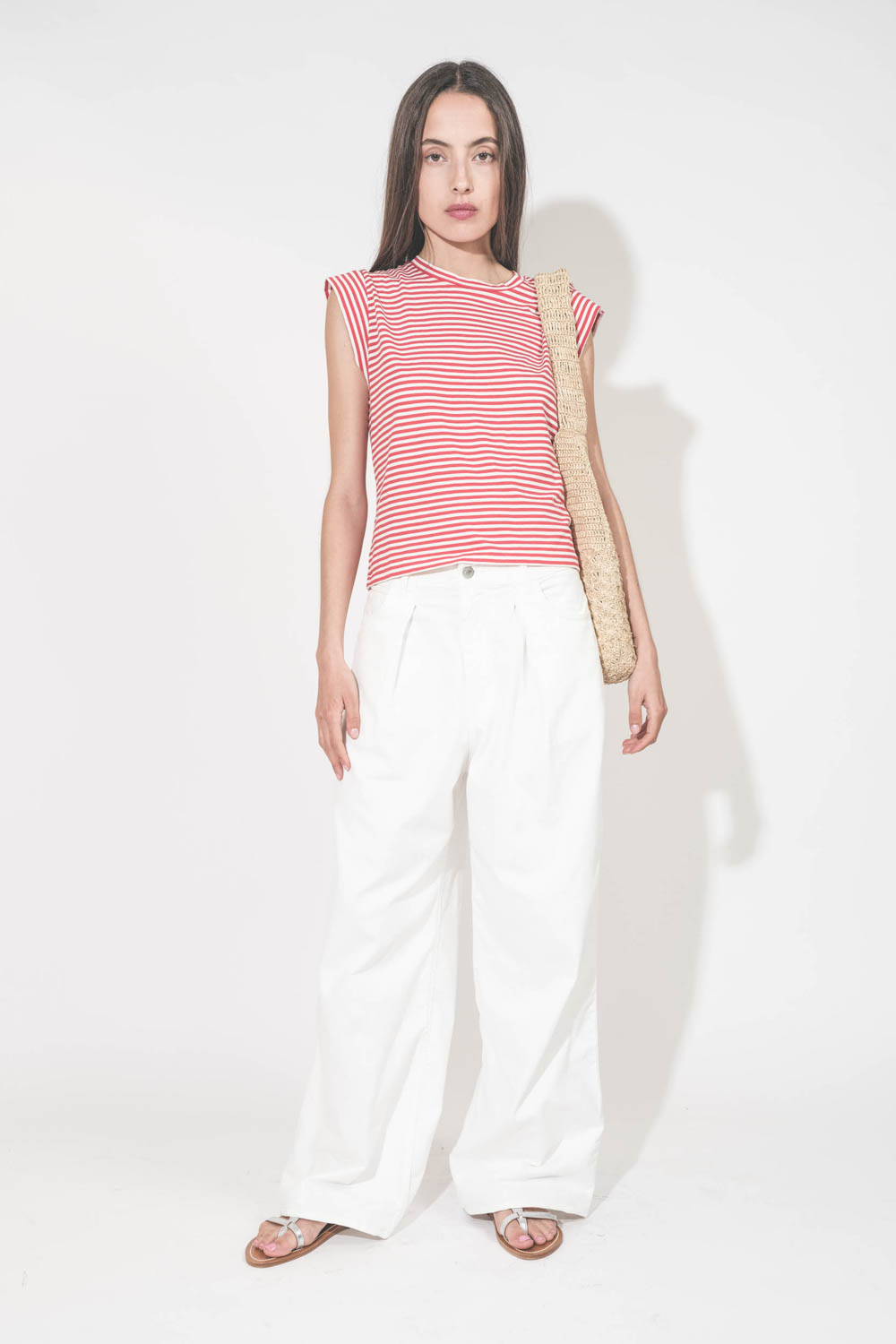 Tee-shirt manches courtes raccourcies en coton rayé rouge et blanc Peak Shoulder The Great. Porté avec un jean large blanc Georgia Denimist et des sandales en cuir argent Caravelle K.Jacques St-Tropez. Panier en osier naturel Praia Isabel Marant.