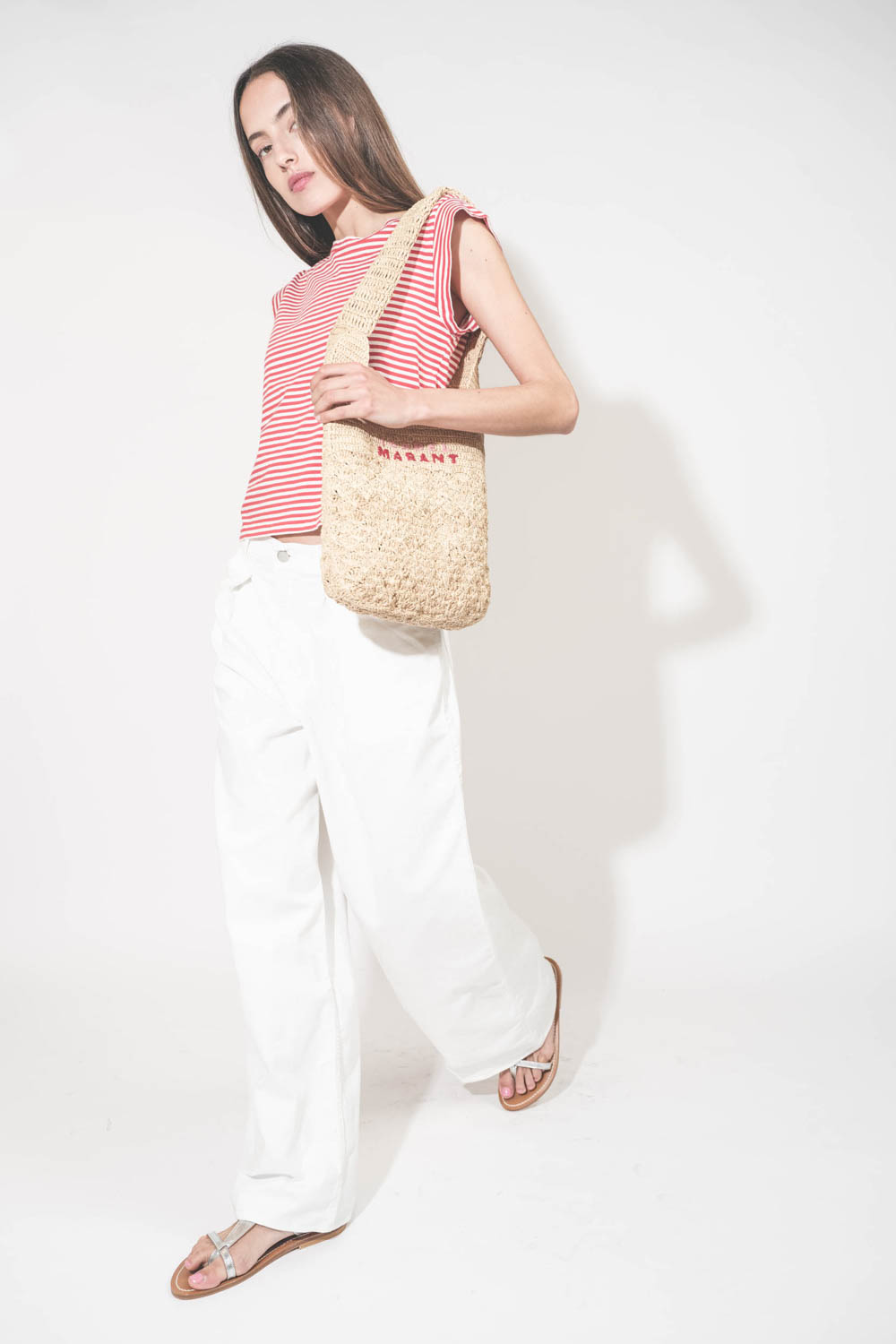 Tee-shirt manches courtes raccourcies en coton rayé rouge et blanc Peak Shoulder The Great. Porté avec un jean large blanc Georgia Denimist et des sandales en cuir argent Caravelle K.Jacques St-Tropez. Panier en osier naturel Praia brodé rose et rouge Isa